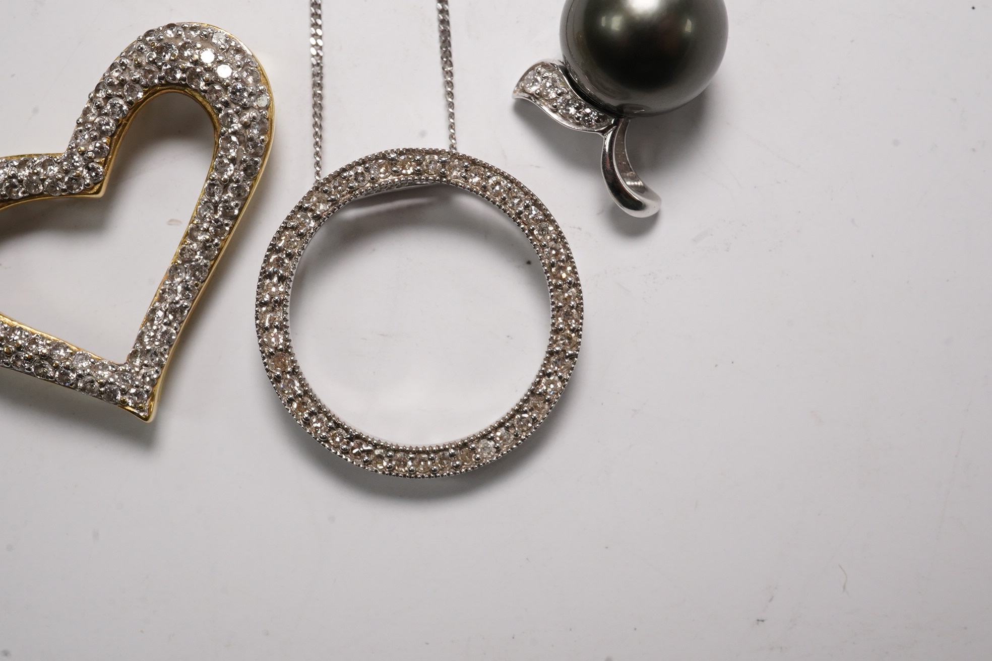 A modern 18k and diamond cluster set open work heart pendant, 25mm, a 9ct white gold and diamond chip set circular pendant necklace and o 9ct and Tahitian cultured pearl set pendant. Condition - fair to good
